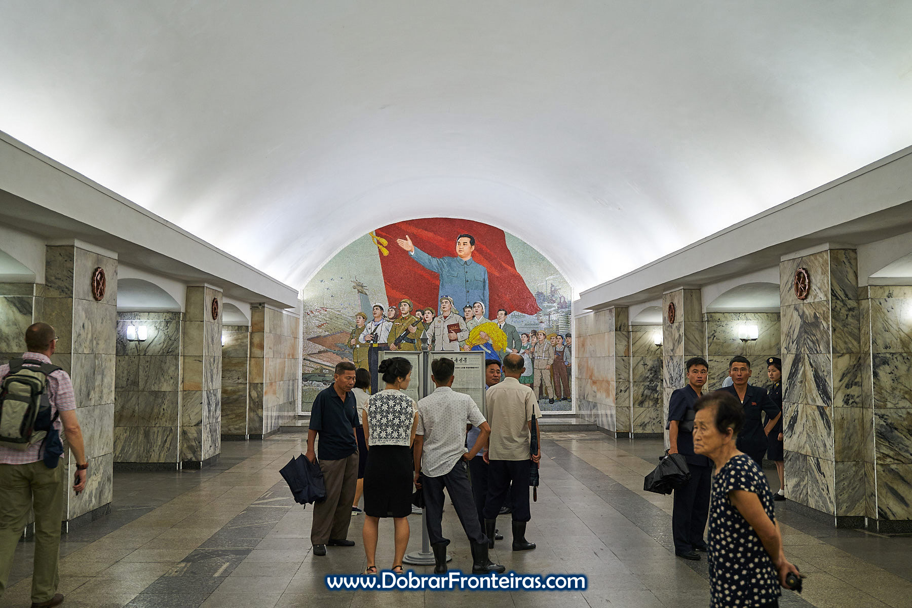 Estação de Pulgunbyol com mural de mosaico com Kim-il-Sung e alguns passageiros a ler jornal