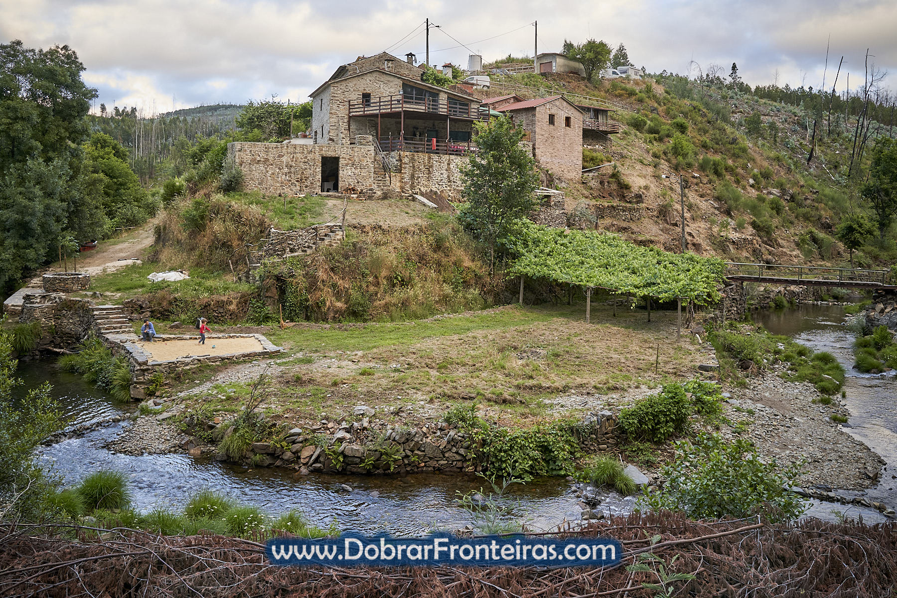 Aldeia de xisto com ribeira e criança a brincar